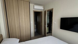 Habitación de hotel con cama, armario, equipo de aire acondicionado y televisor montado en la pared.