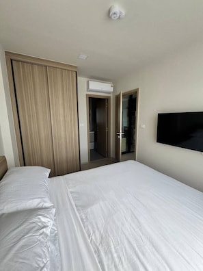 A hotel room with a bed, a wardrobe, an air conditioning unit, and a television mounted on the wall. - The Base • 1BR • Skyline View (Choeng Thale)