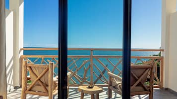 A balcony with a view of the sea, wooden furniture, and a round table.