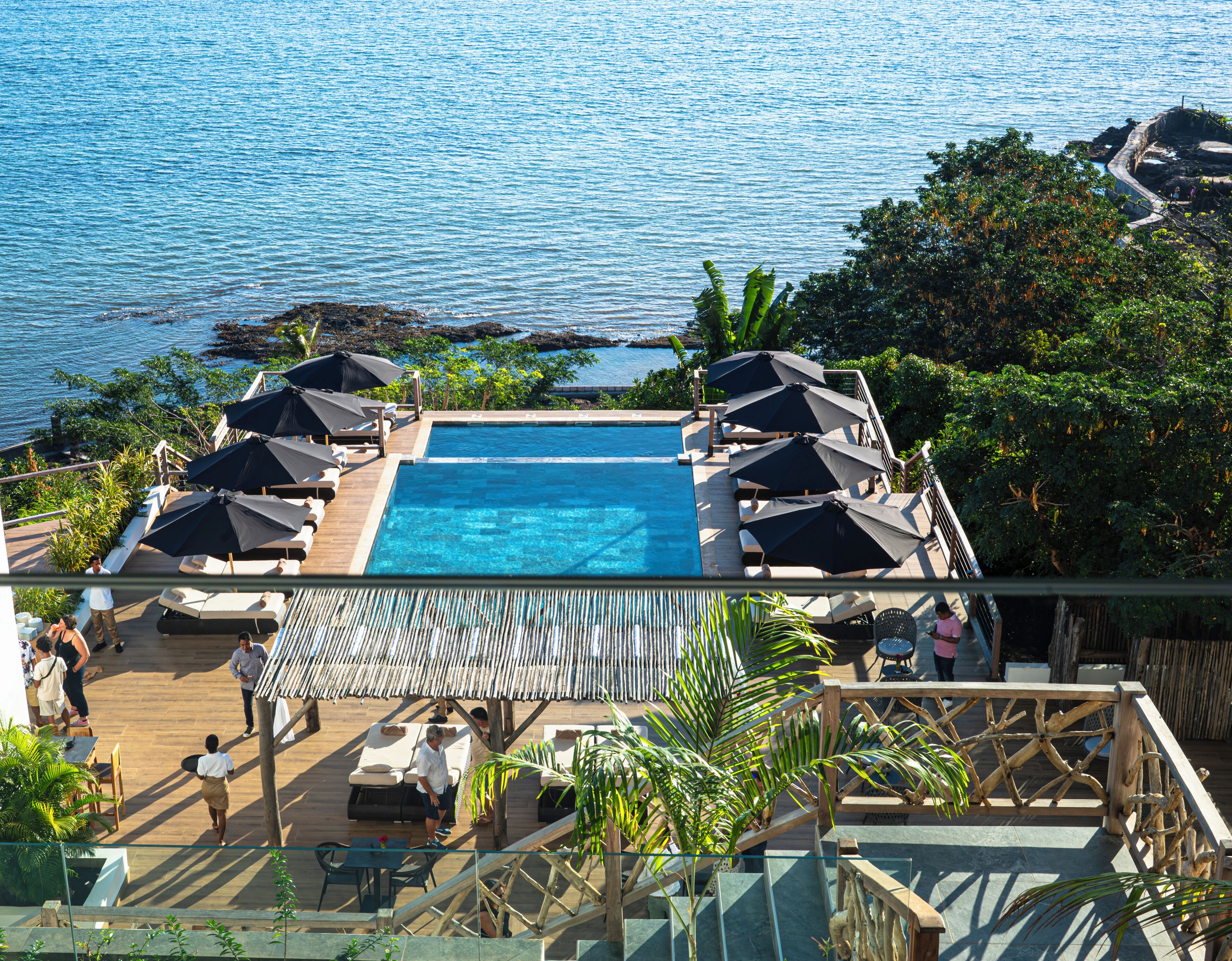 Un espace piscine doté de chaises longues et de parasols, avec vue sur une étendue d’eau.
