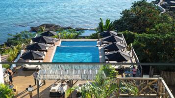 Un espace piscine doté de chaises longues et de parasols, avec vue sur une étendue d’eau.