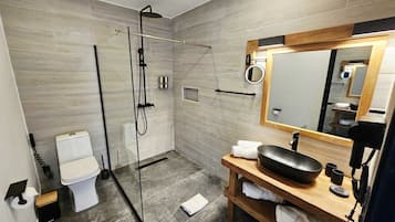 A modern bathroom with a glass-enclosed shower, a white toilet, a wooden vanity with a black sink, and a large mirror.