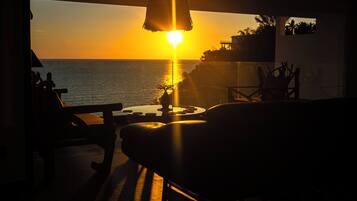 A sunset view from a balcony with a table and chairs, overlooking the sea.