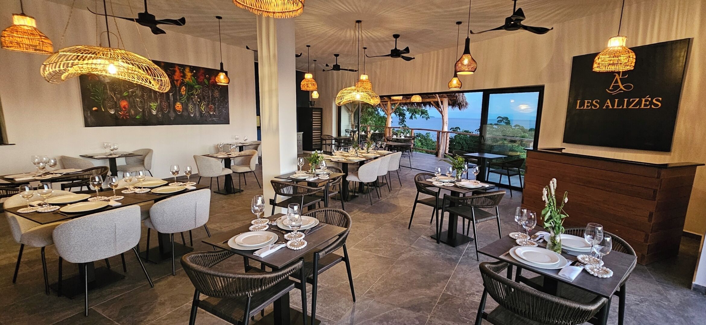 Un restaurant doté de nombreuses tables, de chaises en osier et de lampes suspendues en osier.