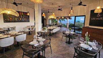 Un restaurant doté de nombreuses tables, de chaises en osier et de lampes suspendues en osier.