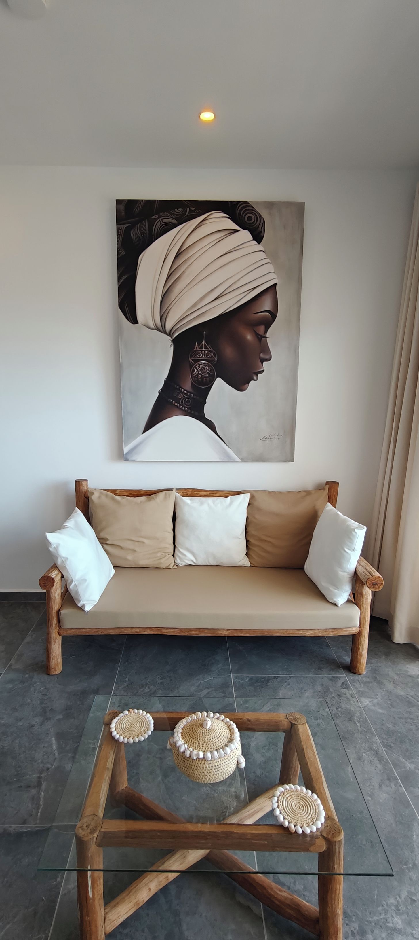 A living room with a sofa, a glass coffee table, and a wall-mounted painting.