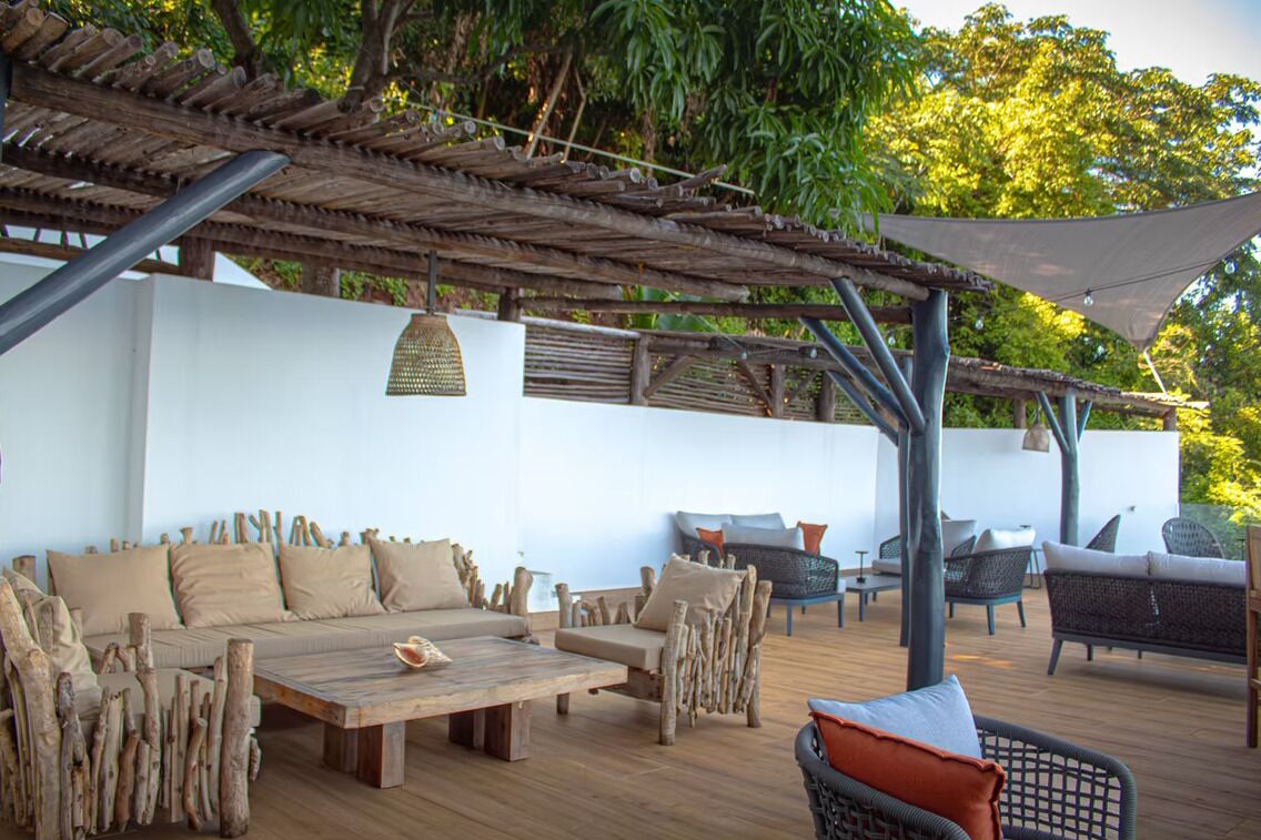 Un espacio exterior con mobiliario de madera y una estructura de pérgola.
