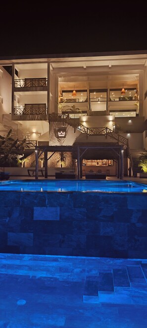 Un edificio de varios niveles con piscina, zona de estar al aire libre y un bar.
