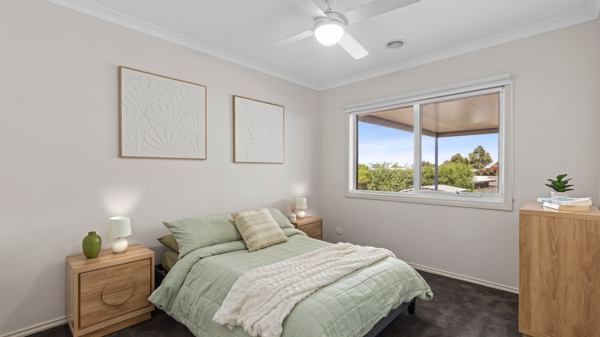 A bedroom with a bed, a nightstand, a lamp, a window with a view, and two wall art pieces.