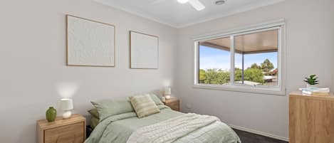Un dormitorio con cama, mesita de noche, lámpara, ventana con vistas y dos obras de arte en la pared.