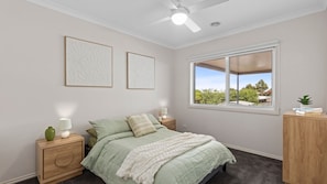 Une chambre à coucher comprenant un lit, une table de chevet, une lampe, une fenêtre avec vue et deux œuvres d’art murales.