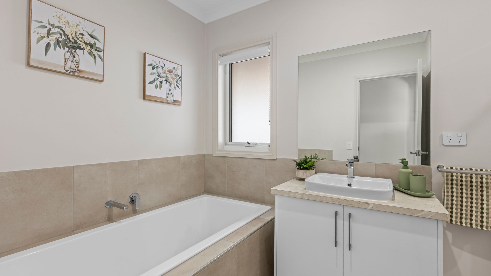 Un baño moderno con bañera, lavamanos y espejo. Dos cuadros con motivos florales decoran la pared.