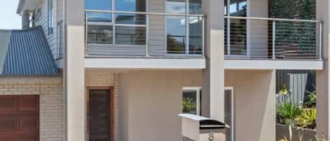 Um edifício residencial de dois andares com varanda, garagem e uma pequena área externa com cascalho.