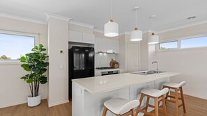 Eine moderne Küche mit einer zentralen Kochinsel, Barhocker, einem Kühlschrank und Pendelleuchten.