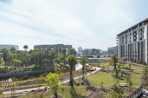 A modern residential area with a central water feature, surrounded by greenery and palm trees. - Park Place | Lush Apartment | Balcony and Lake Views (Cape Town)