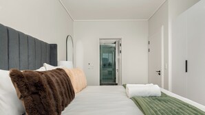 Una camera d'albergo moderna con un letto grande, un comodino, uno specchio e una porta che conduce al bagno.