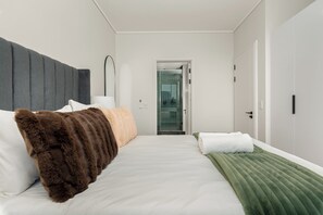 A modern hotel room with a large bed, a bedside table, a mirror, and a door leading to a bathroom. - Park Place | Lush Apartment | Balcony and Lake Views (Cape Town)