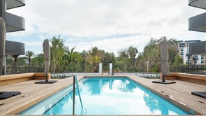 Una piscina rettangolare circondata da un pontile di legno, una recinzione bianca e palme sullo sfondo.