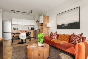 A modern living room with a sofa, coffee table, and a dining area with a kitchen in the background. - Park Place | Lush Apartment | Balcony and Lake Views (Cape Town)