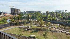 Un parco lungo il fiume con sentieri pedonali, panchine e un cantiere in lontananza.