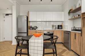 Une cuisine moderne avec des meubles blancs, un réfrigérateur en acier inoxydable, une machine à café et un lave-vaisselle.