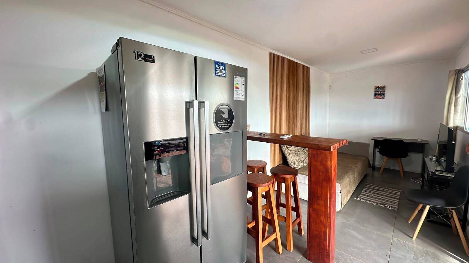 Un espacio habitable compacto con kitchenette, refrigerador, barra de madera y cama.