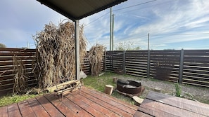 A wooden deck with a metal fire pit, a bench, and a pile of straw.
