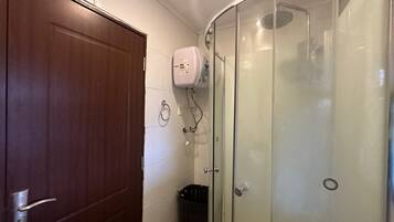 Un baño con puerta de madera, cabina de ducha de vidrio y pared con azulejos blancos.