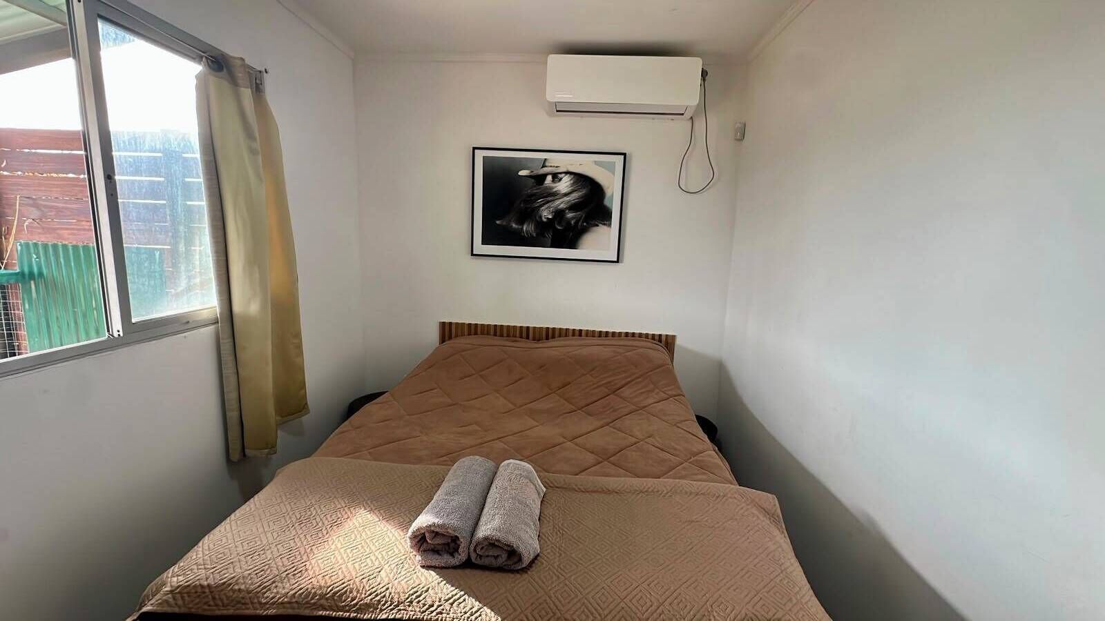 Una cama individual con cabecera acolchada, una toalla enrollada y un cuadro en la pared.