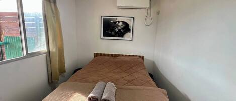 Una cama individual con cabecera acolchada, una toalla enrollada y un cuadro en la pared.