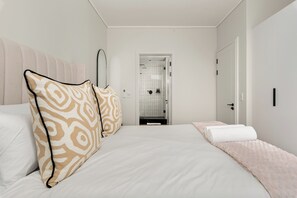 A hotel room with a bed, a bedside table, a mirror, and a door leading to a bathroom. - Park Place, Elegant Retreat with Lake Views (Cape Town)