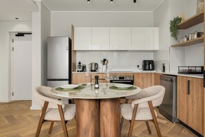 A modern kitchen with white cabinets, a central island with chairs, and a refrigerator. - Park Place, Elegant Retreat with Lake Views (Cape Town)