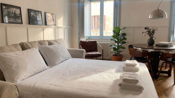 A bedroom with a bed, a chair, a table with a vase, and a window. - Monti Mood Design Apt - via Urbana - Rome (Rome)