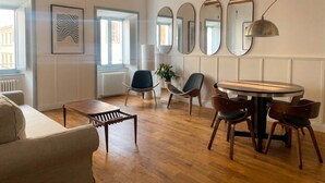 A modern living room with a round wooden table, multiple chairs, a sofa, and a large mirror wall. - Monti Mood Design Apt - via Urbana - Rome (Rome)