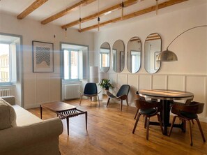 Ein modernes Wohnzimmer mit einem runden Holztisch, mehreren Stühlen, einer Couch und einer großen Spiegelwand.