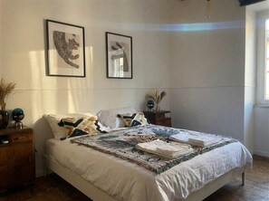 A bedroom with a bed, two framed artworks on the wall, a bedside table with a lamp, and a window. - Monti Mood Design Apt - via Urbana - Rome (Rome)