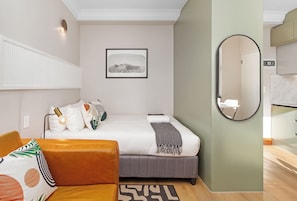 Une chambre d’hôtel avec un lit, une table de chevet, un miroir, un tableau accroché au mur et un tapis à motifs.