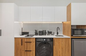Una cocina moderna con armarios blancos, una encimera de madera, un microondas Bosch, un lavavajillas Hisense y una cafetera.