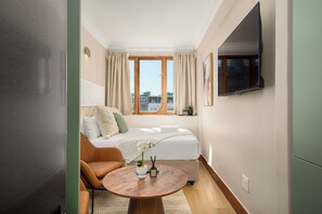 Een hotelkamer met een bed, een stoel, een ronde tafel, een televisie en een raam met gordijnen.