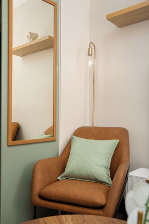 Een kamer met een bruine leren fauteuil, een groen kussen, een hoge vloerlamp en een houten plank.