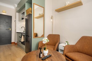 Een moderne woonkamer met een bruine bank, een ronde houten salontafel, een witte orchidee, een afstandsbediening en een spiegel aan de muur.