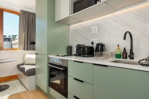 Eine kompakte Küche mit ein eingebautem Backofen, einer Kaffeemaschine und einem Wasserkocher auf der Arbeitsfläche.