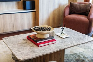 Ein modernes Wohnzimmer mit einem Marmortisch, einer Schale mit Steinen, einem Stapel Bücher und einer kleinen Vase mit Schilfrohren.