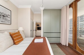 Hotelkamer met een bed, een schilderij, een deur naar een badkamer en uitzicht op een gebouw door een raam.