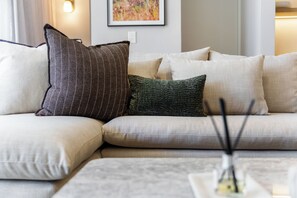 Ein modulares Sofa mit vielen Kissen in einer neutralen Farbgebung, ein kleiner Tisch mit Kerzenhalter und ein gerahmtes Bild an der Wand.