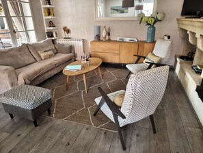A living room with a sofa, armchair, coffee table, and patterned ottoman. - La Zénitude***, a house located 150 m from the Bassin—relaxation guaranteed (Lège-Cap-Ferret)