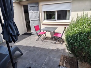 Eine Terrasse mit Tisch und Stühlen, einer Holzbank, einer Tür und einem Fenster.
