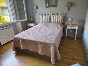 A bedroom with a bed, two bedside tables, a radiator, and a window. - La Zénitude***, a house located 150 m from the Bassin—relaxation guaranteed (Lège-Cap-Ferret)