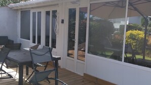 A covered patio with a table and chairs, a large umbrella, and a view of the garden. - La Zénitude***, a house located 150 m from the Bassin—relaxation guaranteed (Lège-Cap-Ferret)