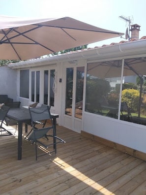 A covered patio with a table and chairs, a large umbrella, and a view of the garden. - La Zénitude***, a house located 150 m from the Bassin—relaxation guaranteed (Lège-Cap-Ferret)